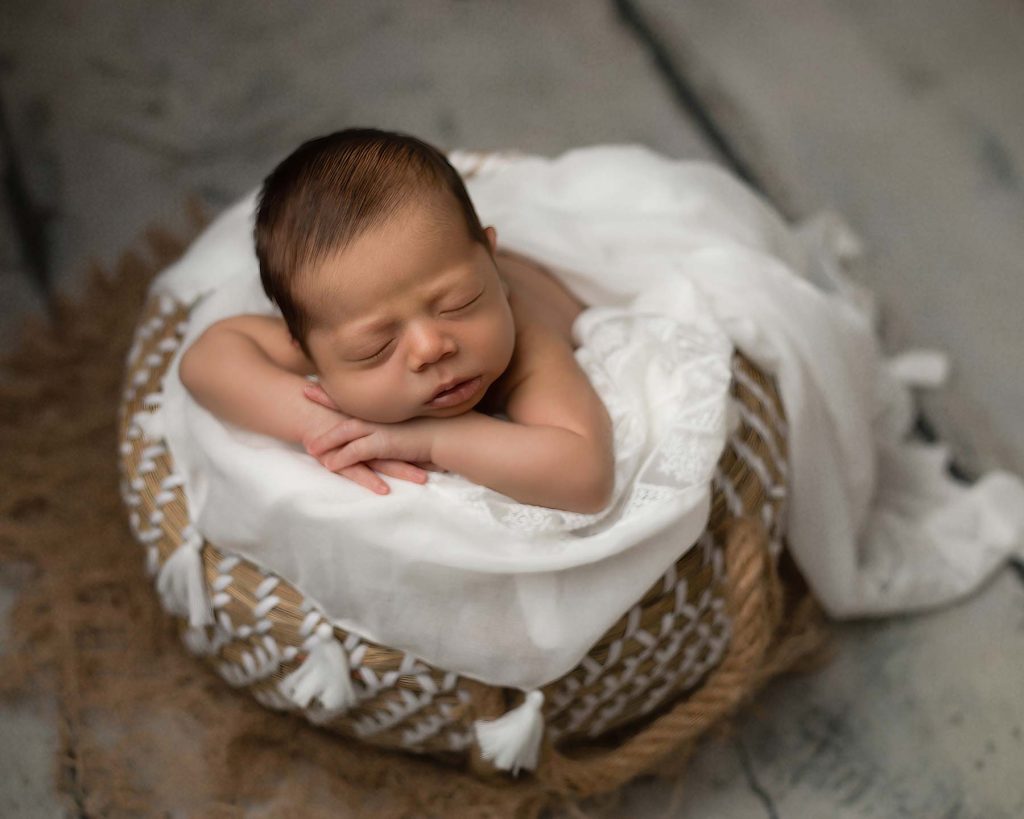 Newborn in pose on white blanket in a cute wicker basket