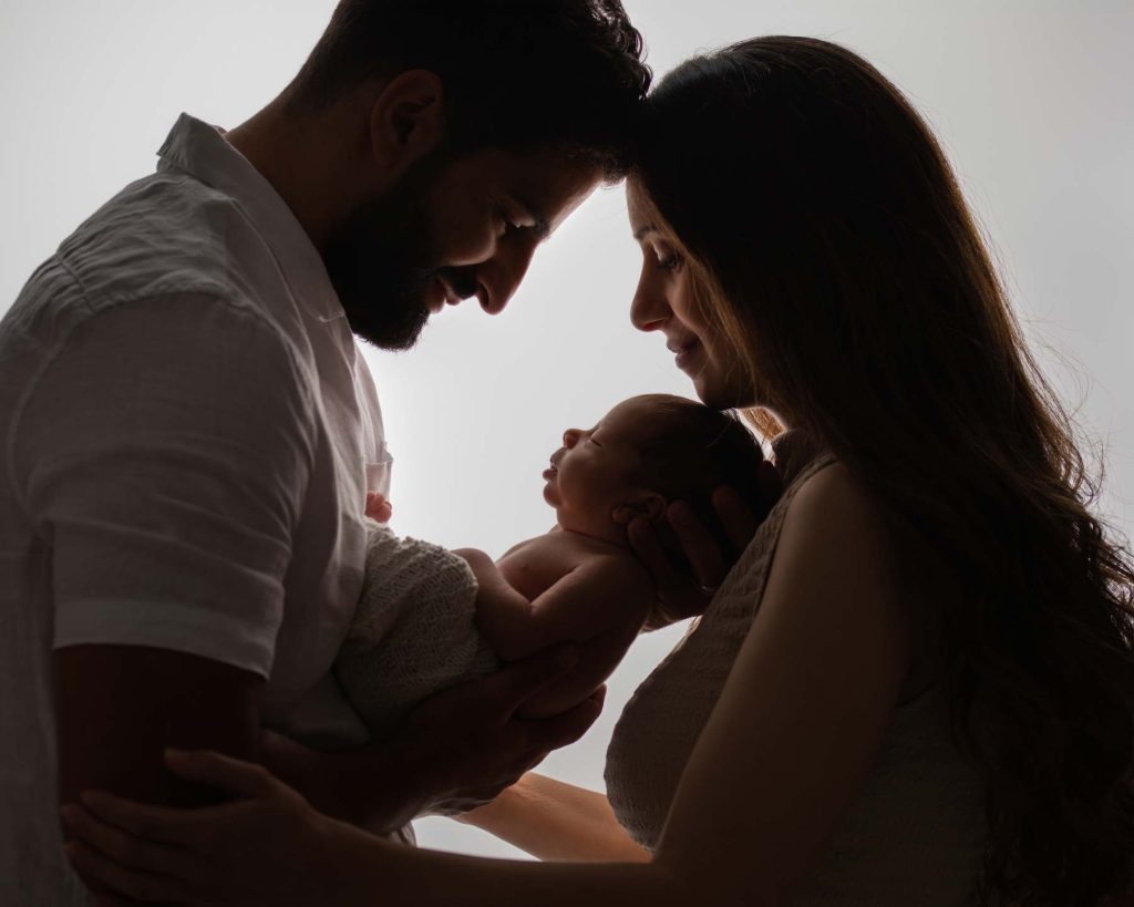 Parents holding their newborn slightly silhouette against a white background