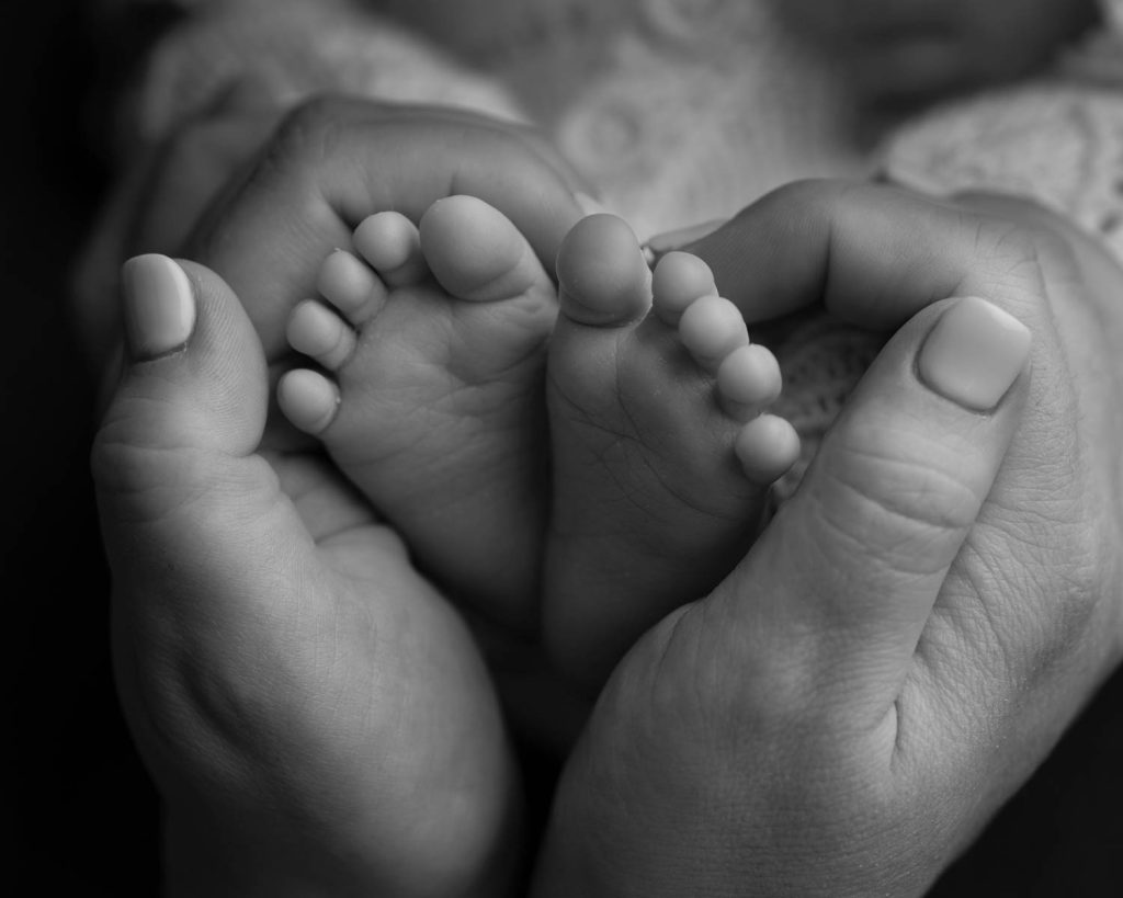 Newborn Photography of adult hands cupping the little feet in black and white.